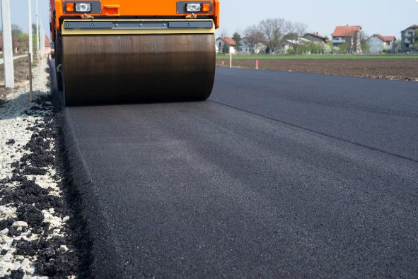 Sealcoating on a commercial parking lot using a tractor and professional equipment.