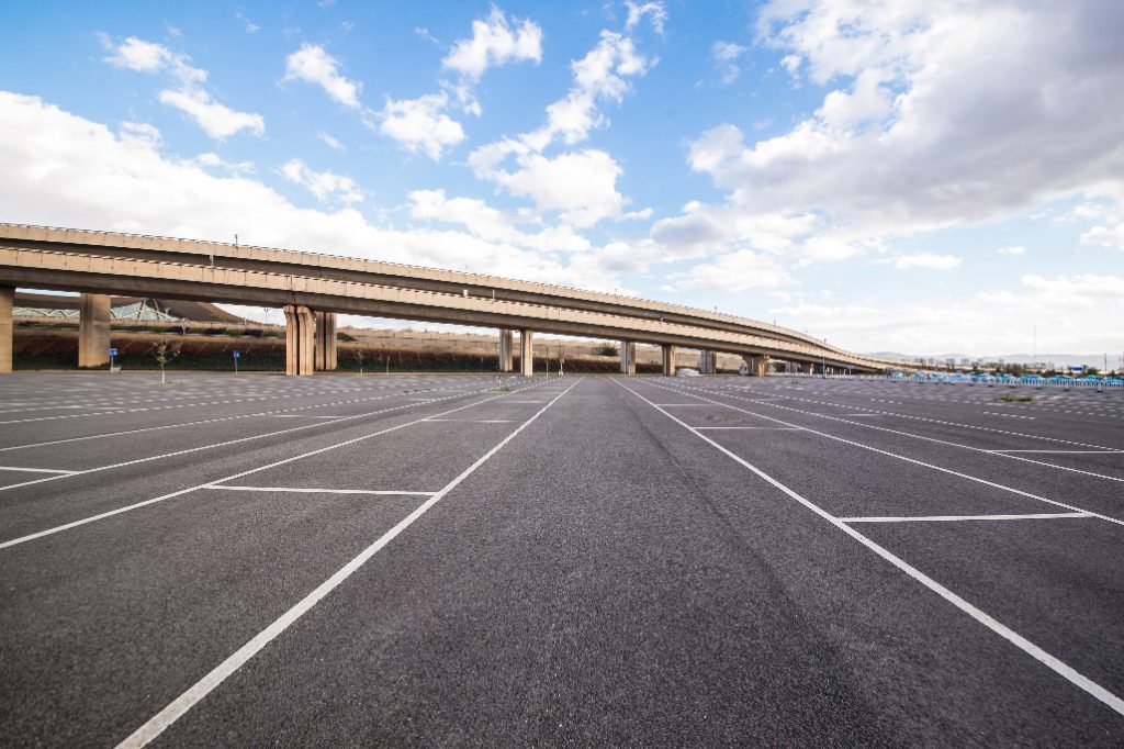 Aerial view of an asphalt parking lot with marked parking spaces and visible vehicle traffic contrast.