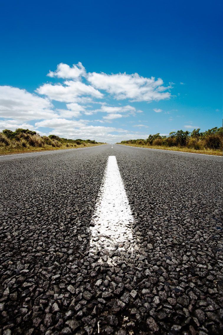 A freshly paved asphalt road stretching into the distance under a clear blue sky.