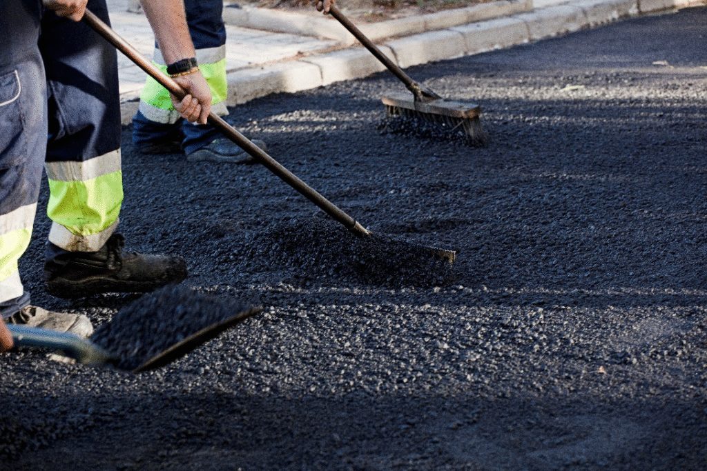 Road worker applying fresh asphalt as part of preventive maintenance to extend pavement life