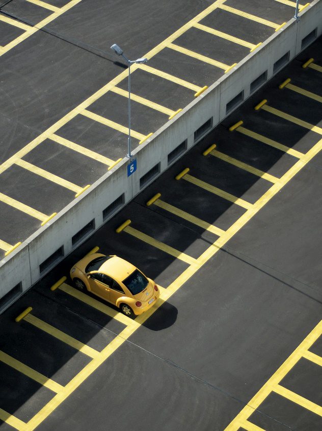 Yellow car parked in a lot with visible wheel stops during daytime.