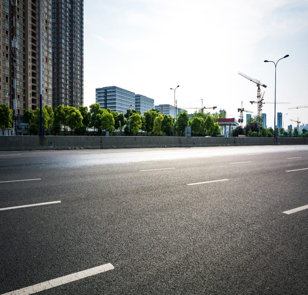 An empty asphalt road in a modern urban square surrounded by tall commercial buildings.