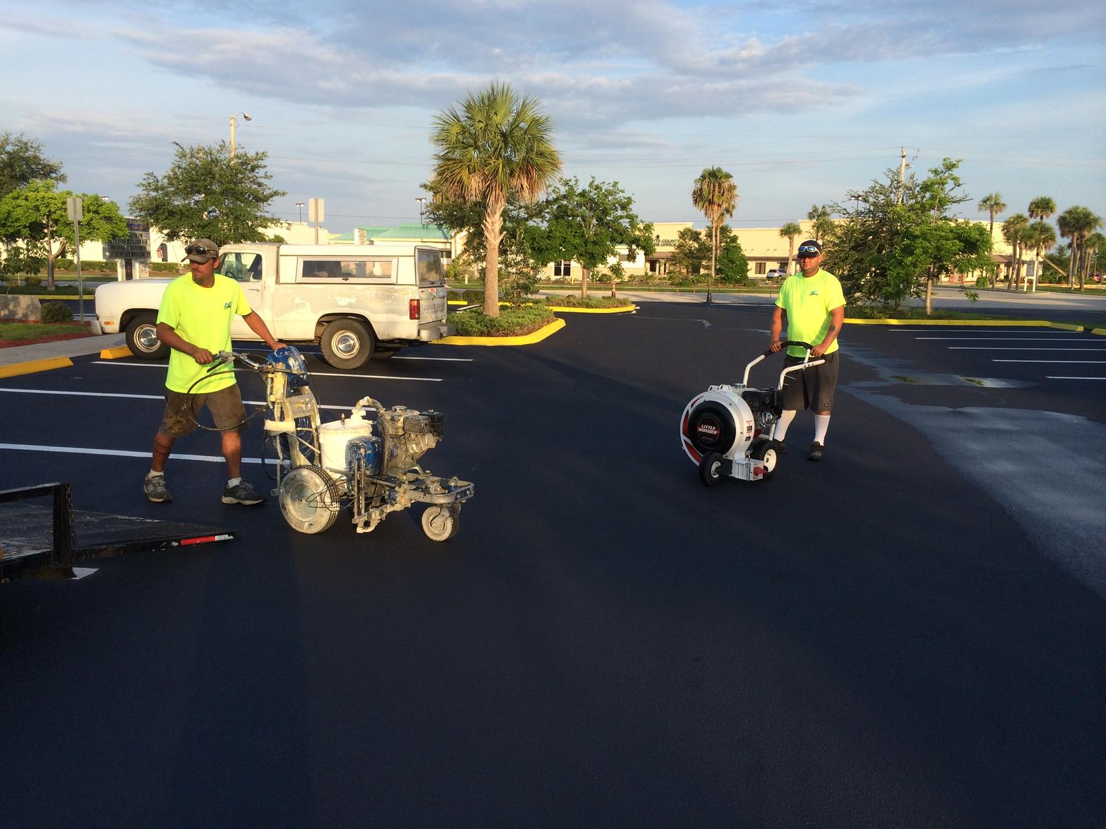 Two crew members striping a freshly sealed lot